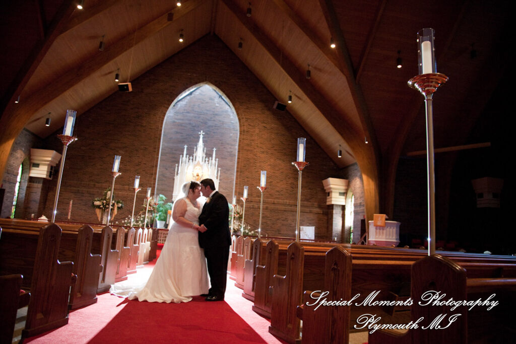A wide-angle interior ceremony photograph looking down the main aisle path frames a backlit wedding couple facing each other before a soaring chancel arch inside Christ Our Savior Lutheran Church in Livonia, Michigan.