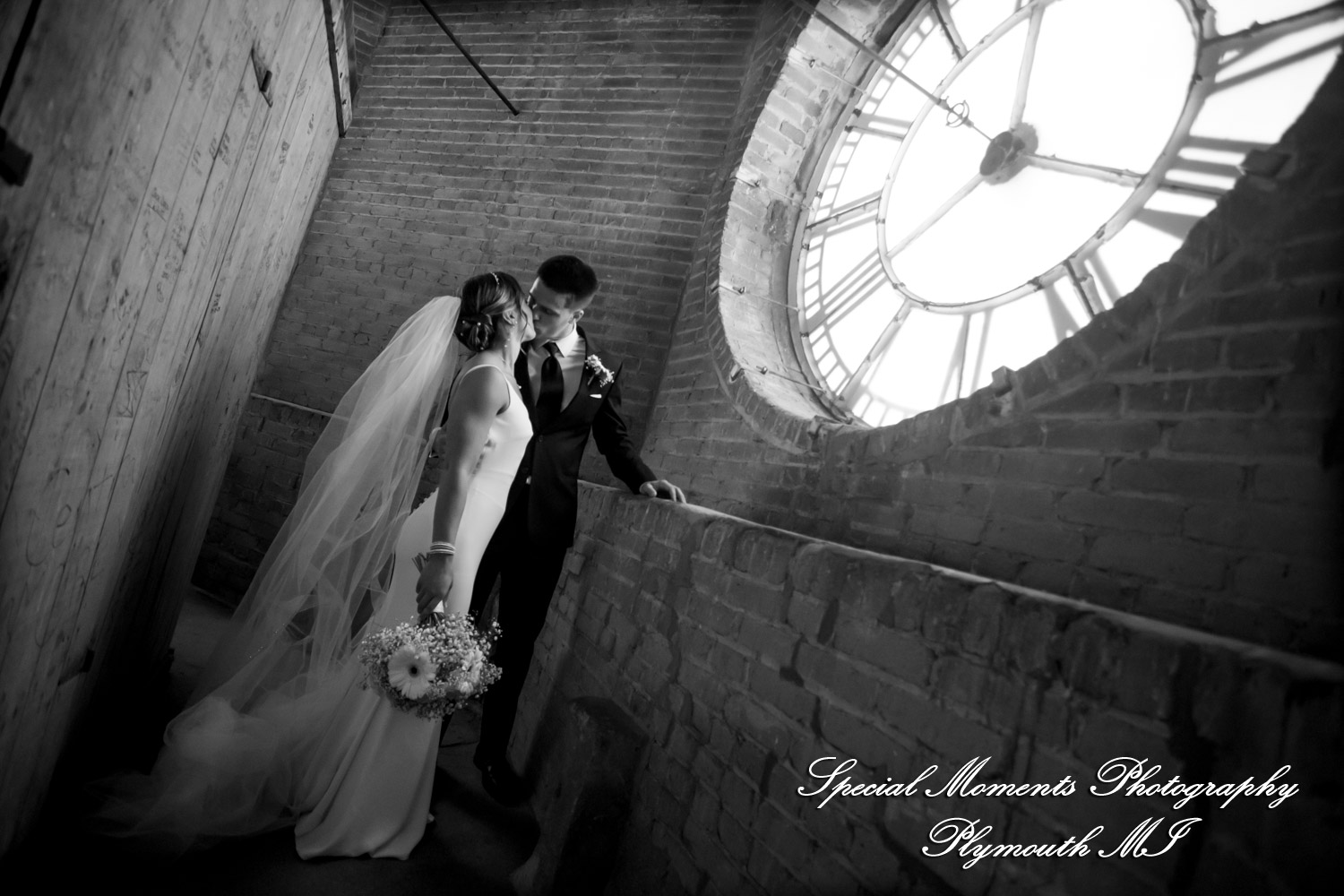 The bride and groom standing at the clock of The Collins at the Clocktower under an overcast Michigan sky